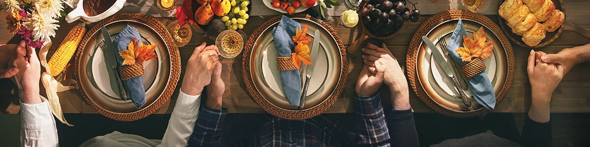 people holding hands in prayer at the dinner table before Thanksgiving dinner