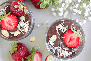 a strawberry chocolate chia mousse in a bowl with fresh strawberries, almonds and coconut flakes